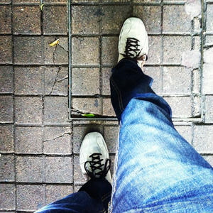 A view looking down at a pair of legs in blue jeans and white sneakers, walking